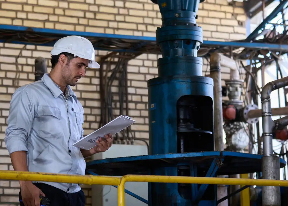 Field engineer reviewing technical documents and supervising industrial plant equipment.